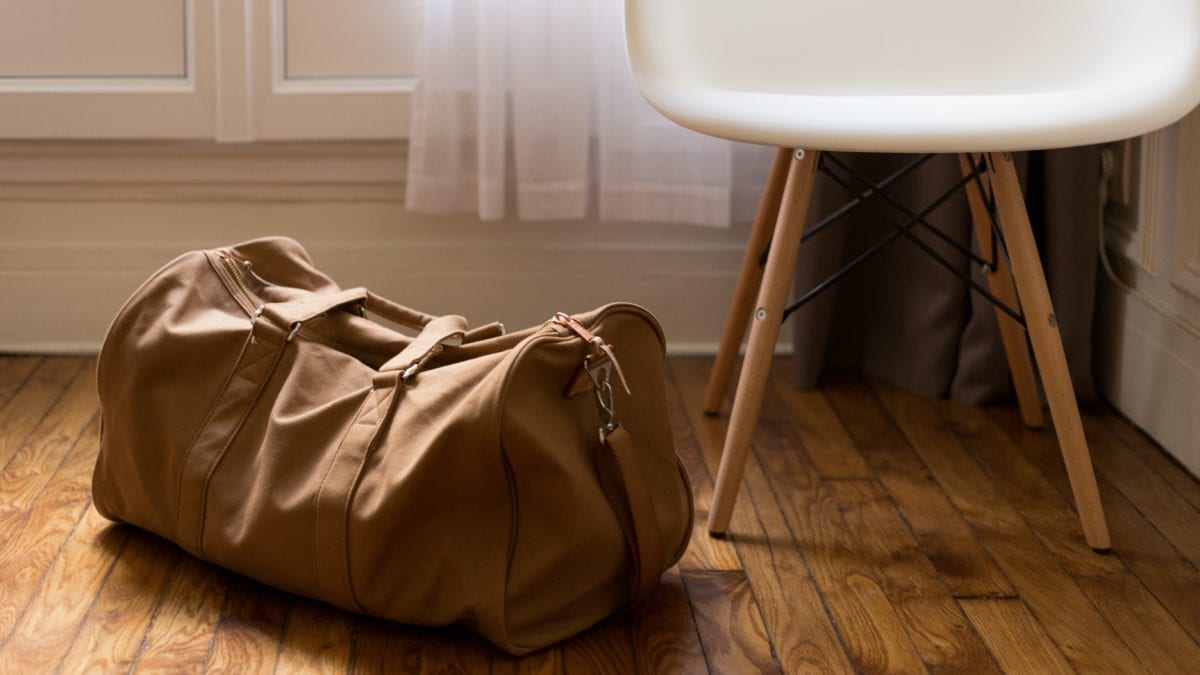 Brown duffel bag beside white and brown wooden chair ... but we are looking for an orange duffel bag