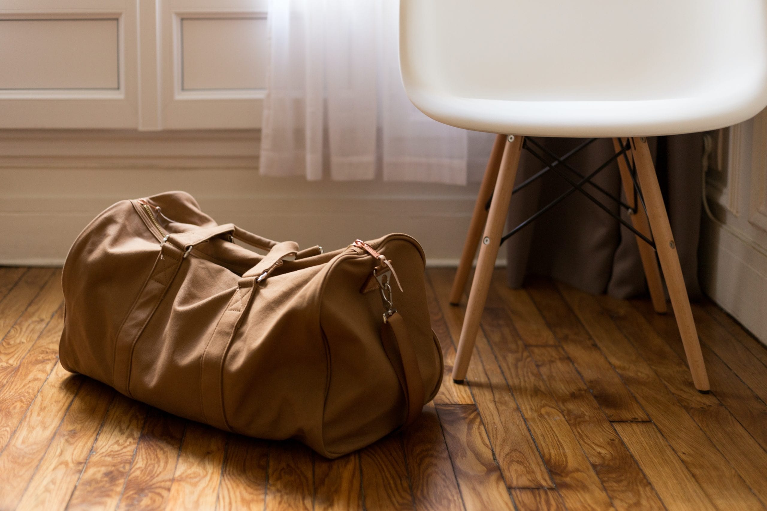 Brown duffel bag beside white and brown wooden chair ... but we are looking for an orange duffel bag