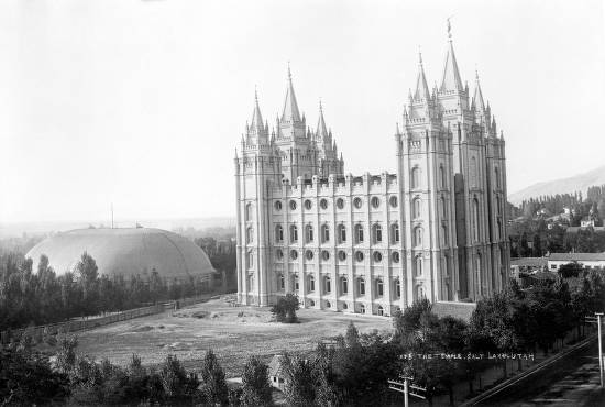View of the Mormon (Latter-Day Saints) Temple at Salt Lake City, Utah; Tabernacle roof visible; railroad track in foreground.