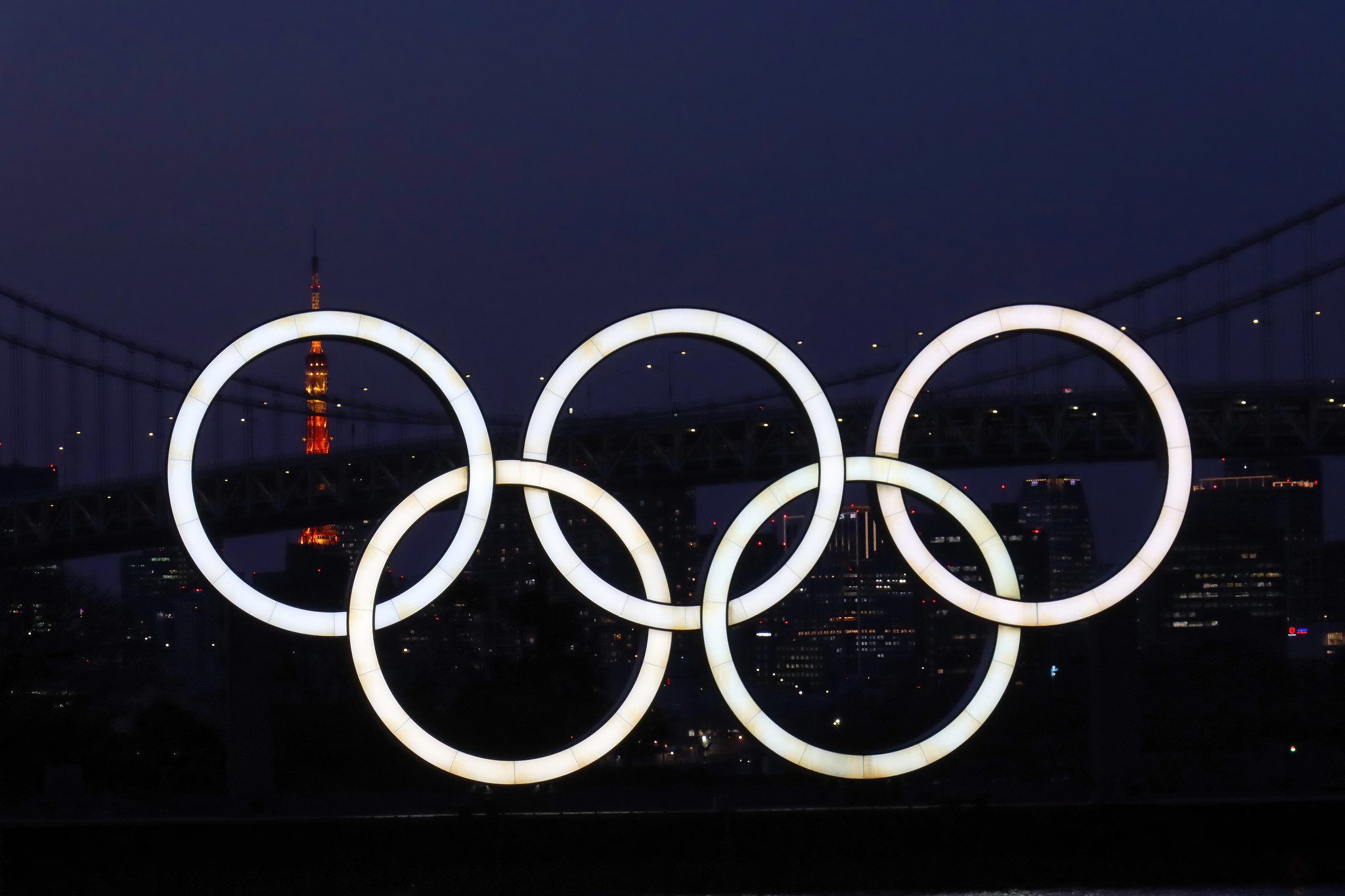 Tokyo 2020 Olympic rings with Rainbow Bridge and the Tokyo Tower in the background.