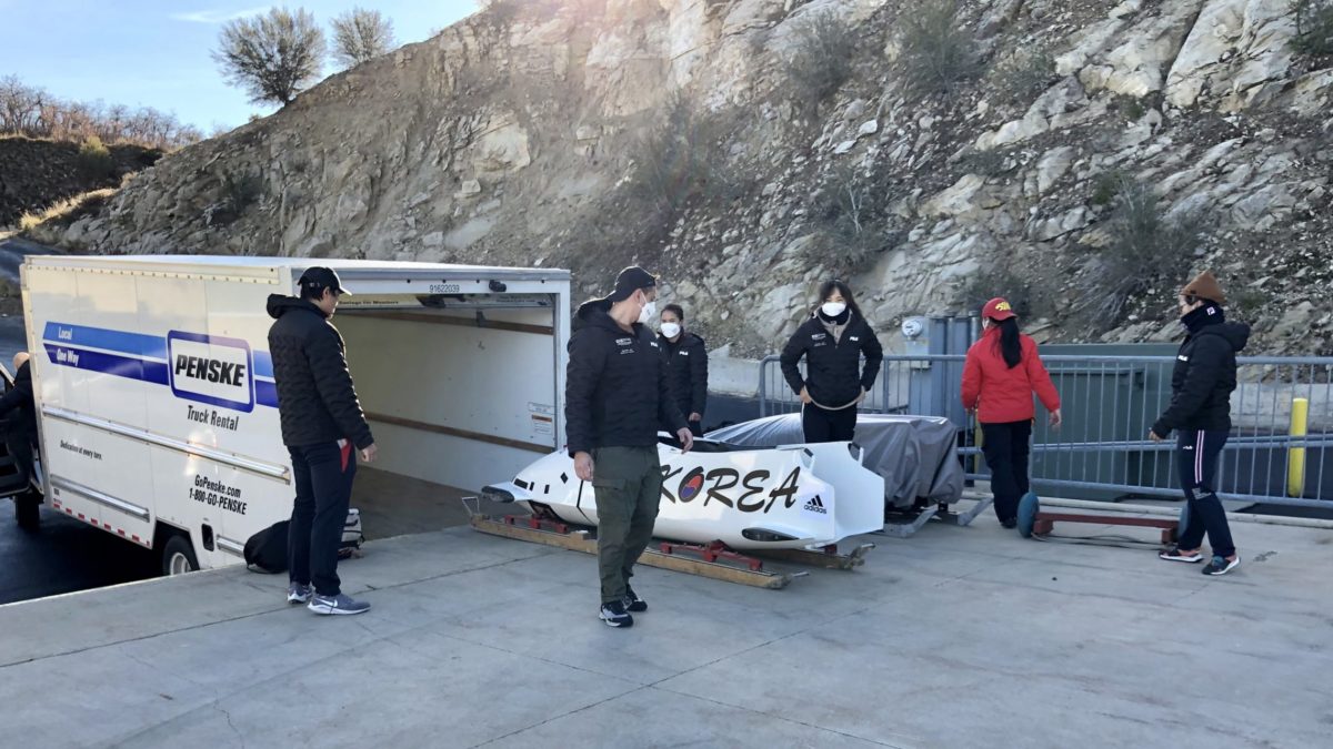 The Korean 2-person bobsled is unloaded at the top of the Park City sliding track as the sun rises over the hill behind it.