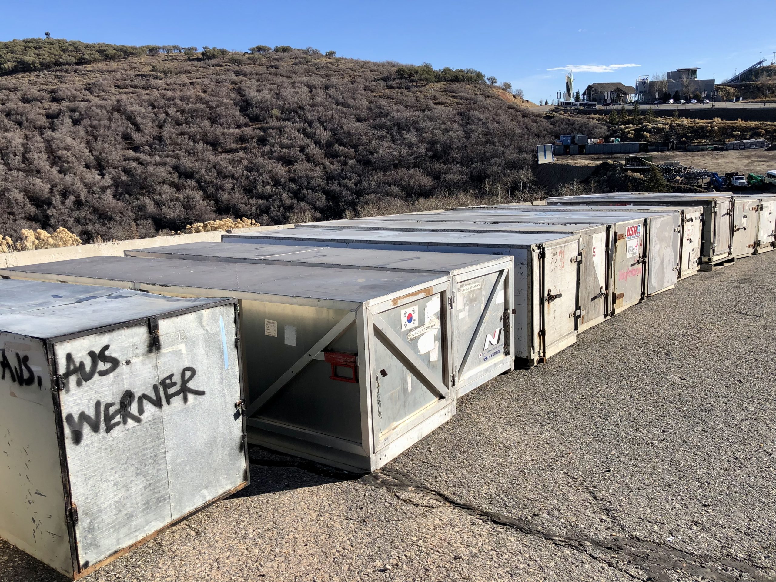 Bobsled international travel crates sit on the sidelines at the Utah Olympic Park while their contents race down the track.