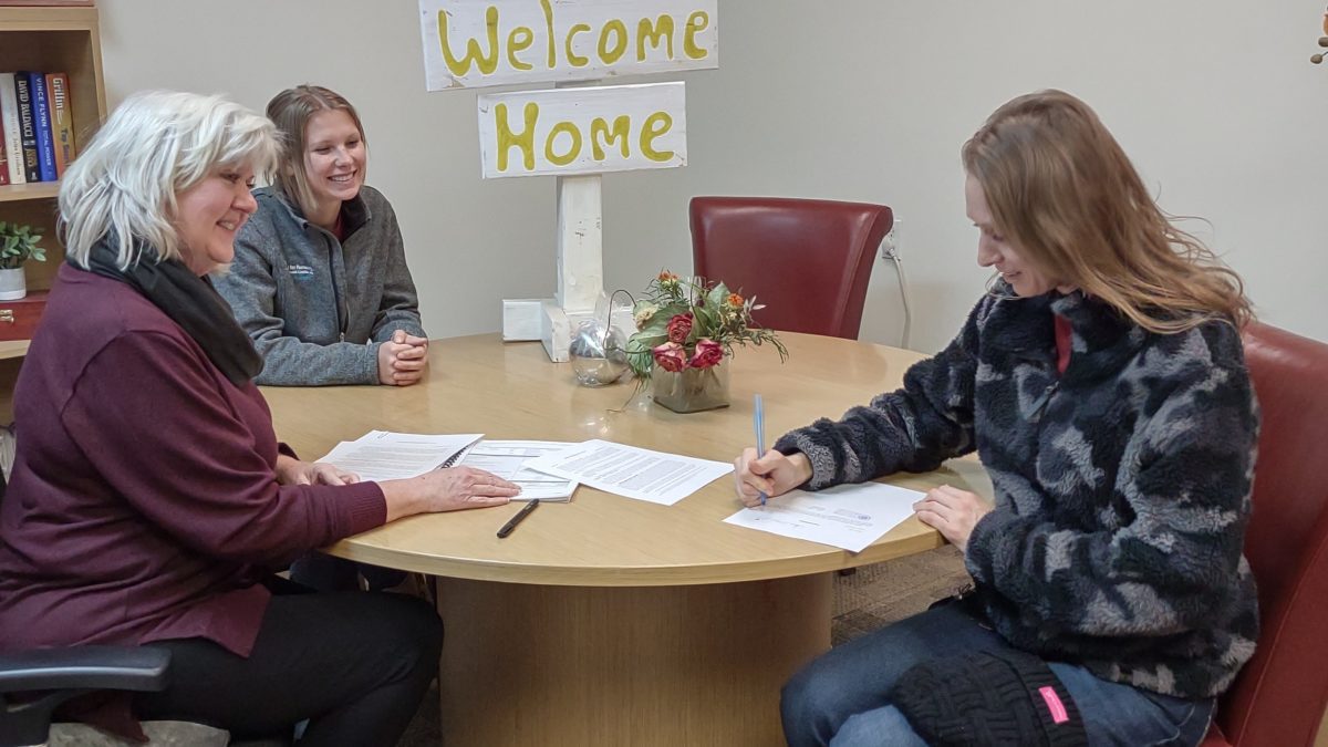 Shellie Barrus and Emily Johnson of Habitat for Humanity watch as Anna May signs papers for her new home.