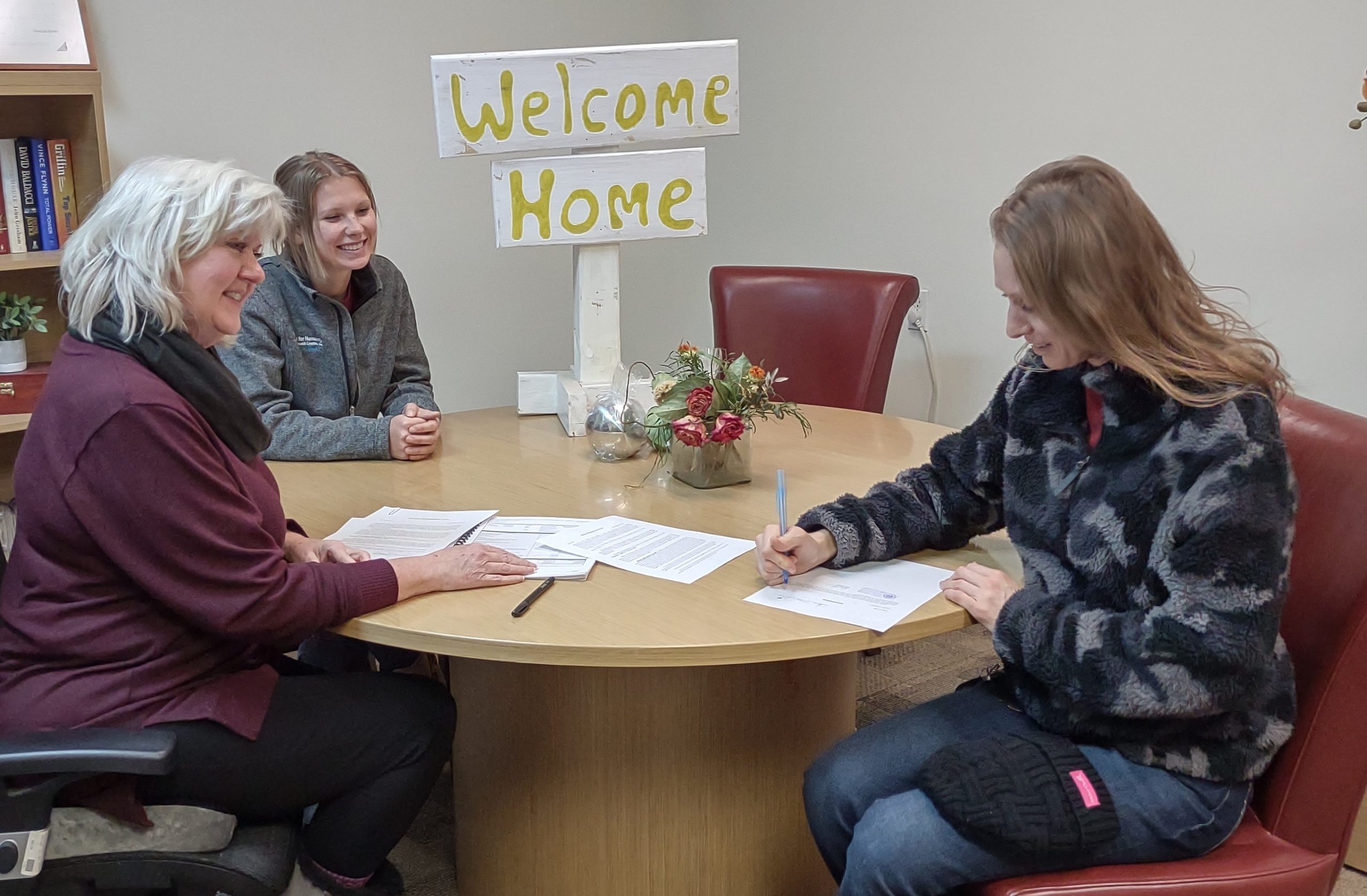 Shellie Barrus and Emily Johnson of Habitat for Humanity watch as Anna May signs papers for her new home.