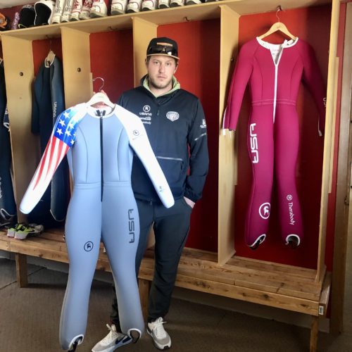 Anders Johnson holding the ski jumping suit he made for Beijing 2022 Olympian Anna Hoffman and standing next to the suit he made for Josie Johnson.