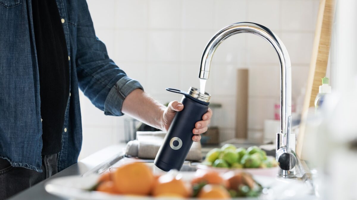 Person holding a bottle under a stainless steel faucet.