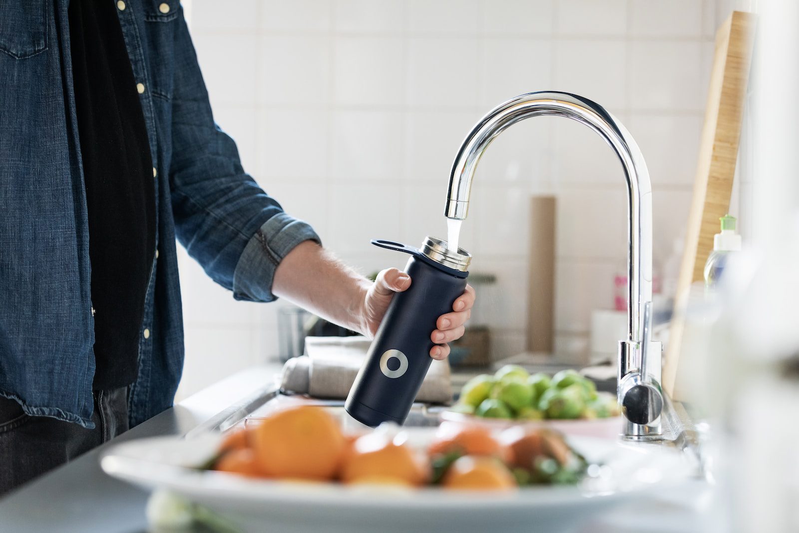 Person holding a bottle under a stainless steel faucet.