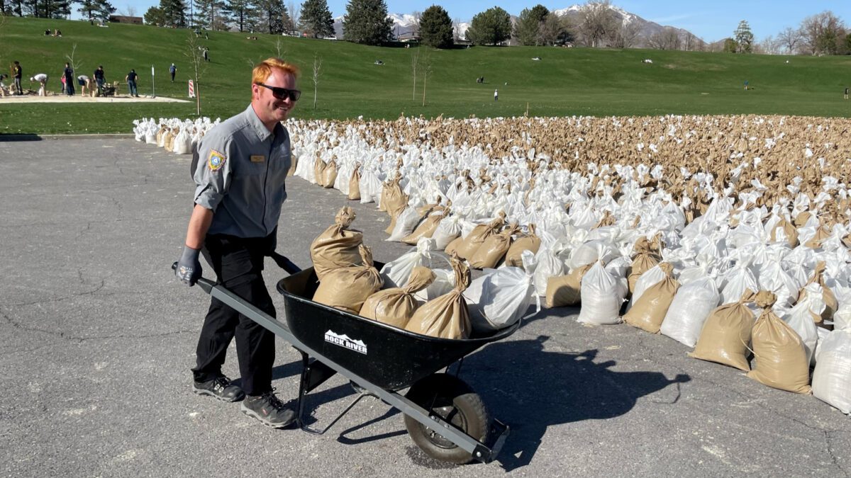 A Salt Lake City Public Lands staff member using to a wheelbarrow to move filled sandbags.