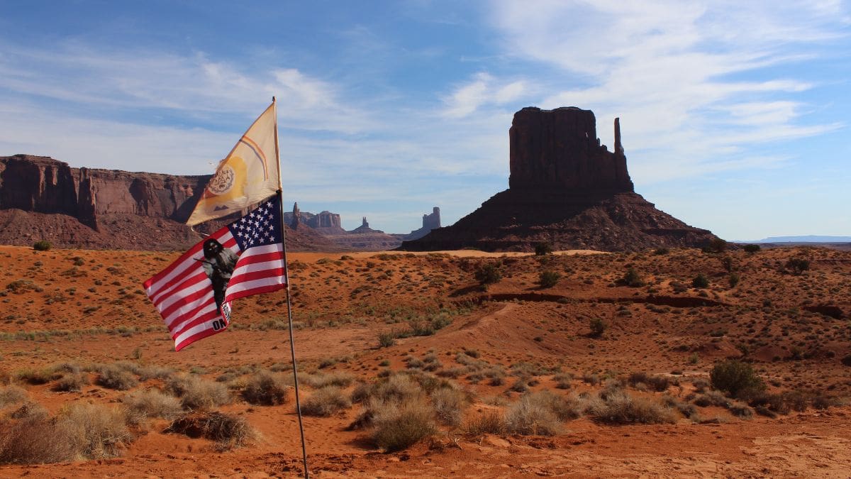 The Navajo Nation and American flags fly in Monument Valley.