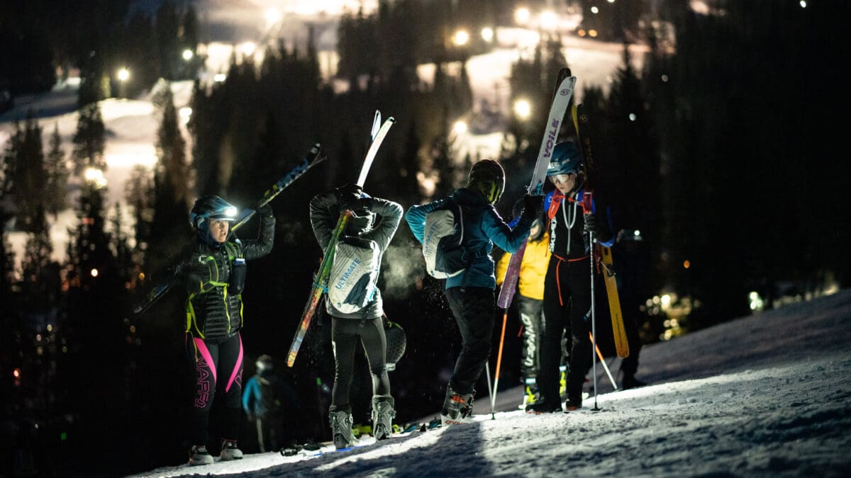 Youth athletes quickly attach their skis to their packs to make their way up a booter.