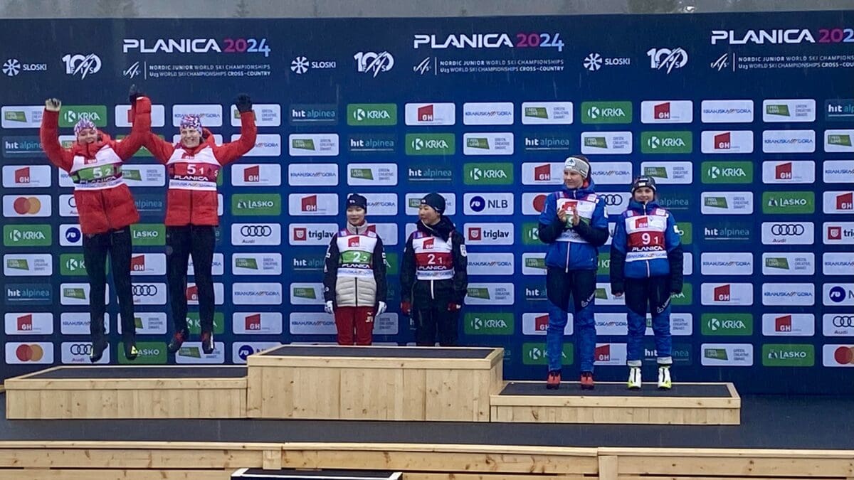 USA Nordic's Kai McKinnon and Alexa Brabec (from far right) jump for joy onto the podium after jumping and skiing into Nordic Combined Team second place at Slovenia's FIS Nordic Junior World Ski Championships.