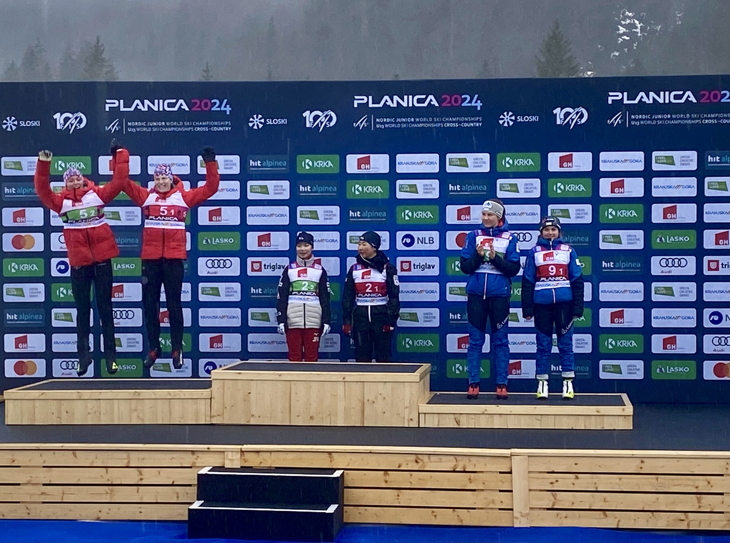 USA Nordic's Kai McKinnon and Alexa Brabec (from far right) jump for joy onto the podium after jumping and skiing into Nordic Combined Team second place at Slovenia's FIS Nordic Junior World Ski Championships.