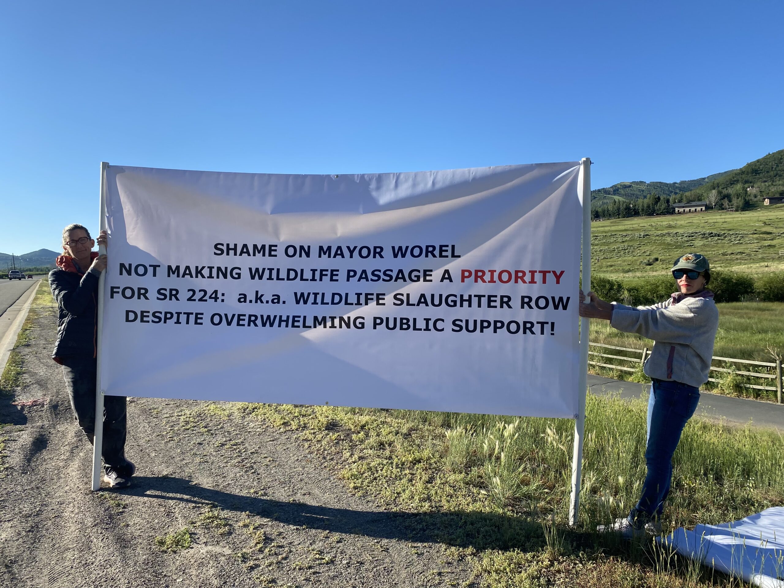 Community members holding up a banner on 224 condemning Mayor Worel's inaction on a 224 wildlife crossing.