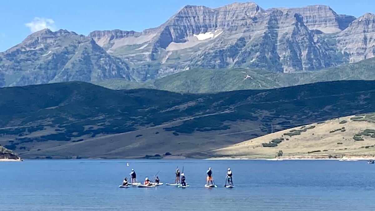 Stand Up Paddle Boarders at Deer Creek Reservoir on a ski instructor professional development day with one of Utah's last remaining patches of snow in the background.