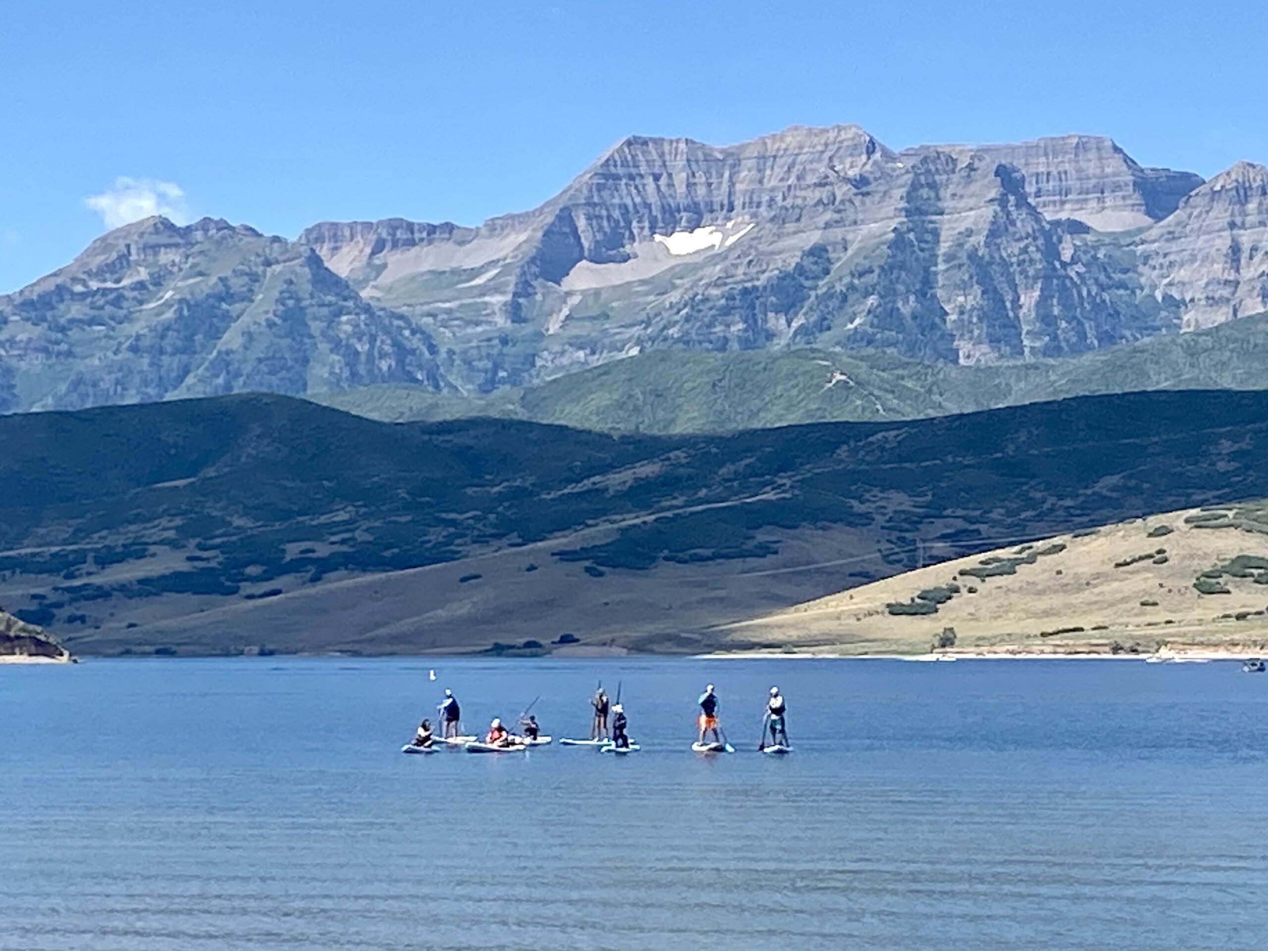 Stand Up Paddle Boarders at Deer Creek Reservoir on a ski instructor professional development day with one of Utah's last remaining patches of snow in the background.