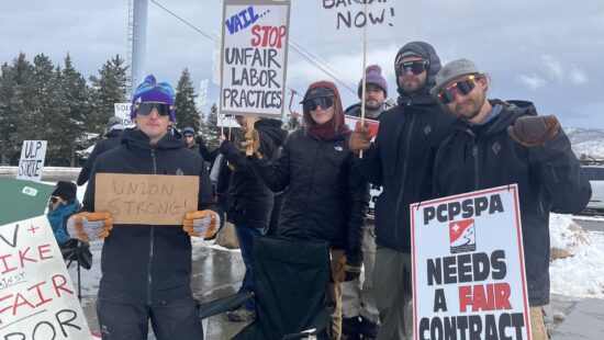 ark City Professional Ski Patrol Association members display signs calling for fair labor practices and a new contract, joined by a furry companion at the picket line near Canyons Resort.