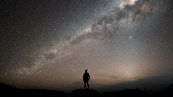 a man standing on top of a hill under a night sky