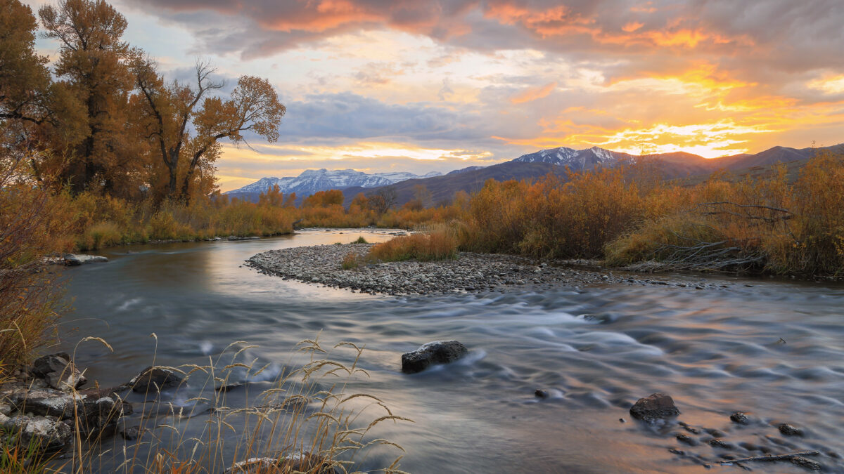 The Provo River winds through autumn foliage beneath a fiery sunset in Heber Valley, with Mount Timpanogos on the horizon—one of many landscapes safeguarded by Utah Open Lands.