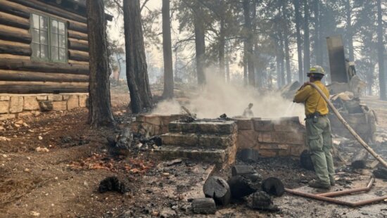 July 13: A firefighter stands near smoldering debris and active flames amid the charred remains of a burned structure near the Grand Canyon Lodge.