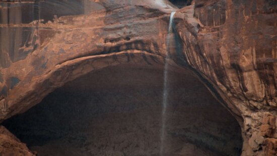 A summer waterfall spills over a cliffside in Arches National Park.