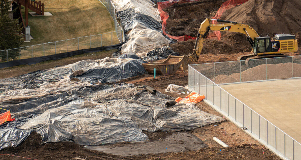 Eastern edge of the project site, where what appears to be a storm drain and adjacent ditch are visible, partially covered with plastic sheeting during demolition work.