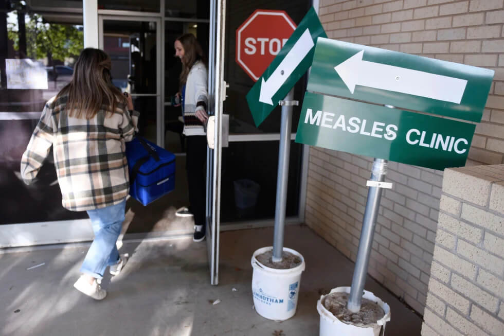 Health department staff members enter the Andrews County Health Department measles clinic carrying doses of the measles, mumps and rubella vaccine, Tuesday, April 8, 2025, in Andrews, Texas. (AP Photo/Annie Rice, File)
