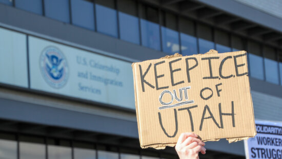 A protester holds a sign outside a U.S. Citizenship and Immigration Services field office in Salt Lake City on Monday, Dec. 8, 2025. (McKenzie Romero/Utah News Dispatch)