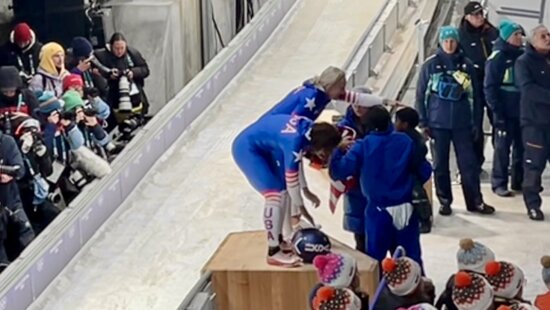 Kaillie Armbruster Humphries and Jasmine Jones bending down after crossing the finish line in first place with only two sleds still to come down the bobsled track, to get a congratulatory hug from teammate Meyers Taylor whose holding one of her young sons.
