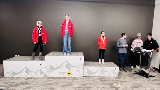(L-R) Park City Ski & Snowboard athletes Lomax McCrank, Andie Brown, and Daisy Schmidt on the all-girls podium of a race announced by Billy Demong and worked on by Eric Camerotta, alongside coaches Adam Loomis, Casey Larson, and Stephen Schumann. Olympians putting medals around the necks of nordic combined and ski jumping competitors on Saturday.
