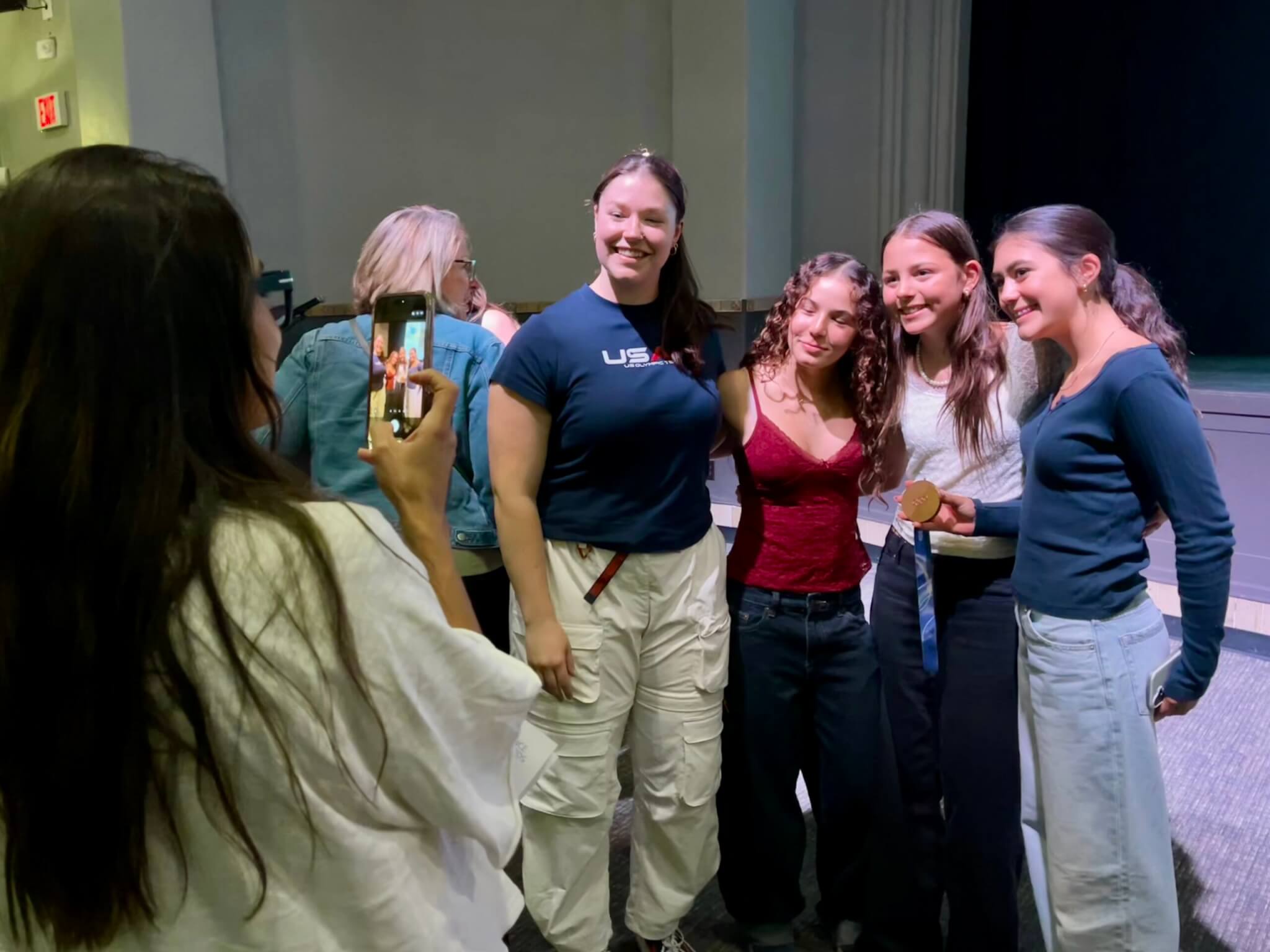 Ashley Farquharson, (blue tshirt) takes photos with fan girls lined up to talk with her and hold her bronze Olympic medal at Youth Sports Alliance event.
