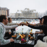 Guests share drinks and food around a patio fire table at the base of Whistler Blackcomb in February 2023.