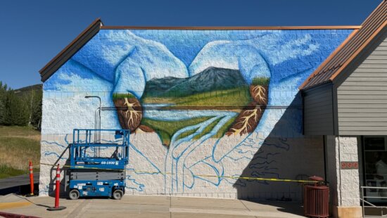 The Junction Commons mural, still in progress, depicts a pair of hands cradling a mountain landscape and reservoir as water flows through the fingers below.