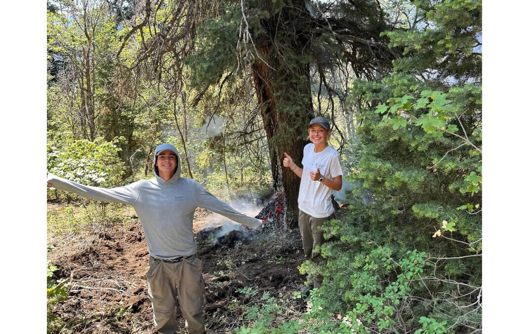 Utah Conservation Corps members Adeline Bondurant, right, and Ethan Fergen, left, stand beside the lightning-struck tree she helped locate at the 910 Ranch on July 21. Park City Fire District crews extinguished the fire before it spread beyond the tree.