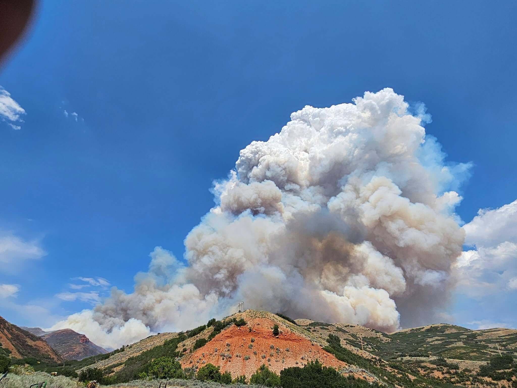 A large smoke column rises from the Rocky Canyon Fire above the red rock hills of the East Canyon area.