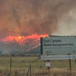 Flames from the Rocky Canyon Fire burn along a hillside behind the East Canyon Wildlife Management Area sign on Sunday, Aug. 9, 2026. Pushed by 40 mph winds and hot temperatures, the fire grew to more than 13,000 acres with 0% containment.
