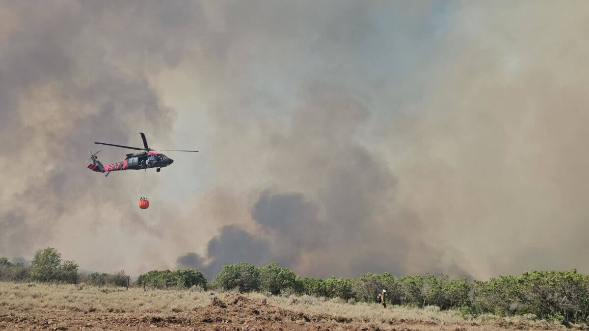 A Utah National Guard Black Hawk helicopter carries a water bucket over the Rocky Canyon Fire as a firefighter works below.