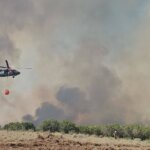 A Utah National Guard Black Hawk helicopter carries a water bucket over the Rocky Canyon Fire as a firefighter works below.