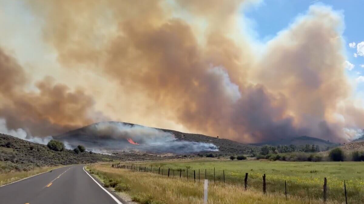 Smoke billows from the Rocky Canyon Fire as flames burn along a hillside near the roadway. Strategic firing operations from the Hogsback to East Canyon Dam held overnight, keeping the fire within its perimeter and protecting East Canyon State Park.