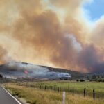 Smoke billows from the Rocky Canyon Fire as flames burn along a hillside near the roadway. Strategic firing operations from the Hogsback to East Canyon Dam held overnight, keeping the fire within its perimeter and protecting East Canyon State Park.