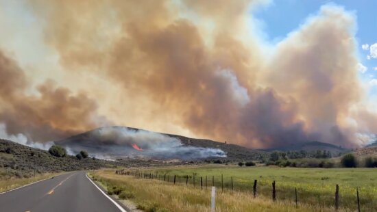 Smoke billows from the Rocky Canyon Fire as flames burn along a hillside near the roadway. Strategic firing operations from the Hogsback to East Canyon Dam held overnight, keeping the fire within its perimeter and protecting East Canyon State Park.