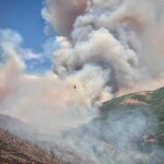 A helicopter conducts water bucket operations over the Rocky Canyon Fire on Saturday, Aug. 8, 2026. The fire grew to an estimated 2,800 acres overnight with 0% containment, and crews are using aviation resources along with dozers and hand crews to secure the fire perimeter.