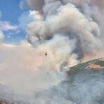 A helicopter conducts water bucket operations over the Rocky Canyon Fire on Saturday, Aug. 8, 2026. The fire grew to an estimated 2,800 acres overnight with 0% containment, and crews are using aviation resources along with dozers and hand crews to secure the fire perimeter.
