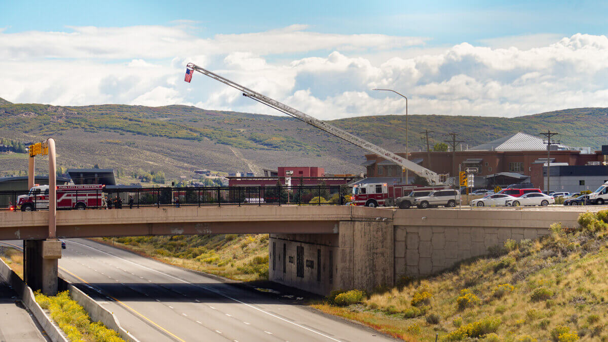 Park City Fire District crews fly an American flag from a ladder truck over Interstate 80 ahead of the procession bringing fallen helicopter pilot Ryan Cutter home to Summit Park on Tuesday, Sept. 29, 2026.